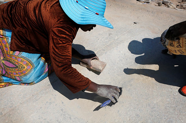 A woman gathering ‘vhovho’ (sand rich in gold particles) as part of her payment for pounding the gold-rich rock. Every particle or grain on the grinding rock is collected as it is believed to contain traces of gold. Women workers claim that they earn at least R500 up to R1 000 per bucket of this kind of sand. Nothing is wasted!