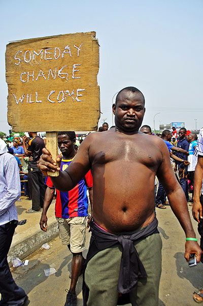 A man poses with a poster which says "One day change will come"