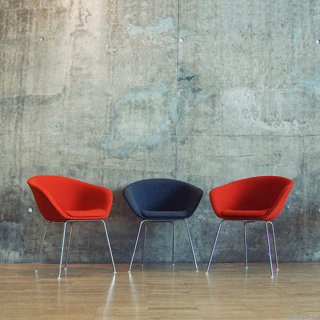 Image of three chairs; two red with one dark grey in the middle
