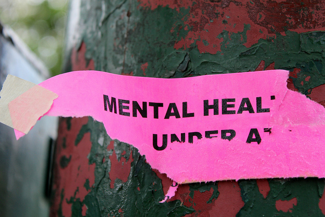 close up of a torn piece of pink paper with words mental heal visible and some partial text on the next line torn which suggests the full message had been 'mental health under attack'