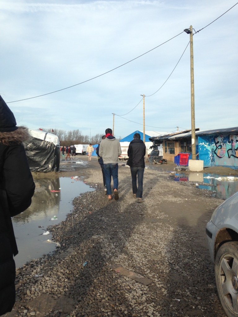 A group of Syrian refugees who fled a war-torn country are walking across the muddy road that runs through the camp